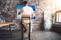 Male painter sits on chair in front canvas and drawing picture in studio. Art class and workshop. Artist painting process