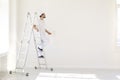 A male painter in a white uniform with a roller works in his hand in a white room