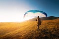 male paraglider takes off from a yellow field with a blue parachute against the backdrop of hills and small mountains Royalty Free Stock Photo
