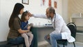 Male pediatrician checking little girl head temperature with his hand and giving her thermometer Royalty Free Stock Photo