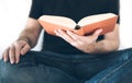 Male person in black shirt and blue jeans sitting on sofa reading a book