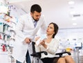 Male pharmacist consulting a woman in a wheelchair in pharmacy