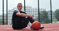 Male player sitting on basketball sports ground with ball. Concentrated sportsman looking at camera during training. Royalty Free Stock Photo