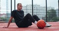 Male player sitting on basketball sports ground with ball. Concentrated sportsman looking at camera during training. Royalty Free Stock Photo