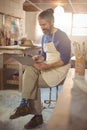 Male potter sitting on stool using laptop Royalty Free Stock Photo