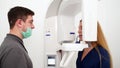 Male radiologist taking teeth x-ray of female patient using dental x-ray machine. Dentist adjusts scan projection by
