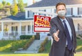 Male Real Estate Agent Reaching for Hand Shake Wearing Medical Face Mask with Sold For Sale Sign Behind