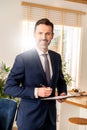 Male real estate broker smiling to the camera, standing in home with documents file