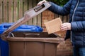 A male recycler placing a cardboard box into a brown roadside recycling bin