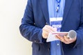 Journalist with press pass at news conference or media event, holding microphone, writing notes Royalty Free Stock Photo