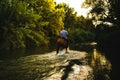 Male riding a horse through a river in the forest in summer