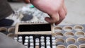 Male`s hand puts cylindric metallic pins into wooden box with round holes.