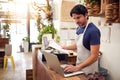 Male Sales Assistant Working On Laptop Behind Sales Desk Of Florists Store Royalty Free Stock Photo