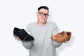 Male salesman with glasses shrugs, showing two different shoes in his hands, on light background. Choice concept Royalty Free Stock Photo