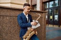 Male saxophonist poses with saxophone at building