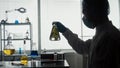 A Male Scientist Holds An Erlenmeyer Flask With A Plant Inside And Examines It. Dark Silhouette Of A Scientist With A