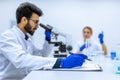 Male scientist working with microscope, doctor's team in laboratory doing research, making notes Royalty Free Stock Photo