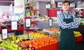 Male seller posing with apples, tangerines and bananas in store