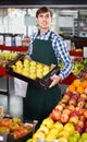 Male seller posing with apples, tangerines and bananas in store