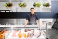 Male seller with seafood at fish shop fridge