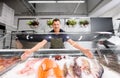 Male seller showing seafood at fish shop fridge