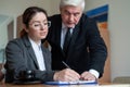 The male senior director watches as the female secretary signs the papers. Business woman fills out documents under the