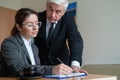 The male senior director watches as the female secretary signs the papers. Business woman fills out documents under the