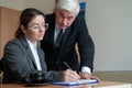 The male senior director watches as the female secretary signs the papers. Business woman fills out documents under the