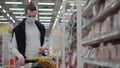 Male shopper is buying up food supply in supermarket, has protective mask