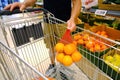 male shopper holding in hand orange fruits in plastic bag, holds ripe orange in hand, puts groceries in iron grocery trolley,