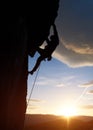 Male silhouette rock climbing at sunrise. Rock climber hanging on cliff above glowing horizon under big cloud. Side view