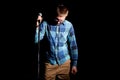Male singer in plaid shirt singing with microphone over dark background