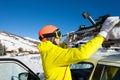 Male skier fastening skis to roof rails of car