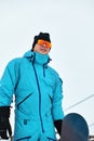 Male snowboarder in a blue suit walking on the snowy hill with snowboard, Skiing and snowboarding concept