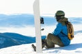 Male snowboarder sitting at the very top of a mountain and taking a look at landscape