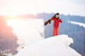 Male snowboarder standing on the top of the snowy hill, holding snowboard in hand, showing thumbs up