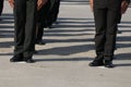 Male soldiers stand in line dressed in uniforms with black cutout shoes outdoors.