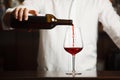 Male sommelier pouring red wine into long-stemmed wineglasses.