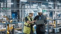 Male Specialist and Female Car Factory Engineer Talking and Working on Laptop and Tablet Computers