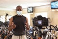 Male sports instructor in gym with a face mask recording video content for online classes, streaming