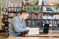 Male student with laptop reading book in the university library Royalty Free Stock Photo