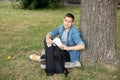 Male student putting books for study into his backpack sit on lawn. Happy Man sitting On Green Grass and study remotely. Royalty Free Stock Photo