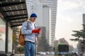 Male student standing at bus stop, looking at route on GPS navigator app map on smartphone.