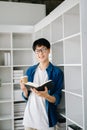 Male student taking notes from a book at library, Young asian sitting at desk doing assignments in college library Royalty Free Stock Photo