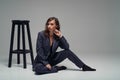 Male style dressed fashion female model. Fashionable woman at male business suit on the black chair posing at studio. Royalty Free Stock Photo