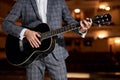 Male in suit plays and sings while standing on stage on a 12-string acoustic guitar