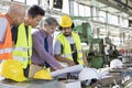 Male supervisor with workers discussing over blueprints in industry Royalty Free Stock Photo