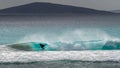 Male surfer crouches catching tube on green wave with offshore breeze causing water spray with hills in the background Royalty Free Stock Photo