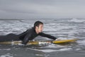 Male Surfer Paddling On Surfboard In Water At Beach