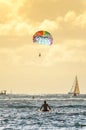 Male surfer sitting on his board looking at a rainbow parasailing parachute in Hawaii Royalty Free Stock Photo